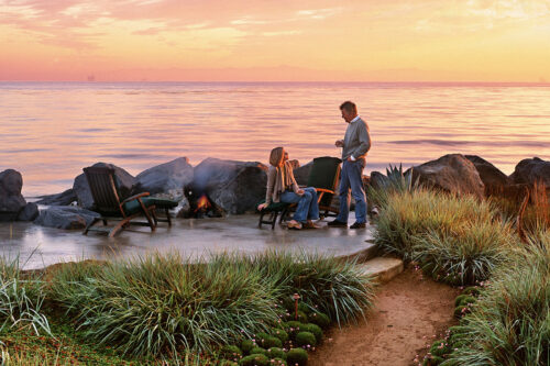 Coastal garden at sunset with native grasses, boulders, fire pit, and ocean views.
