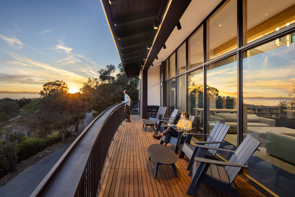 Students relaxing on a curved modern wood deck at Cate School during sunset, featuring architecture by Blackbird Architects and an ocean view.