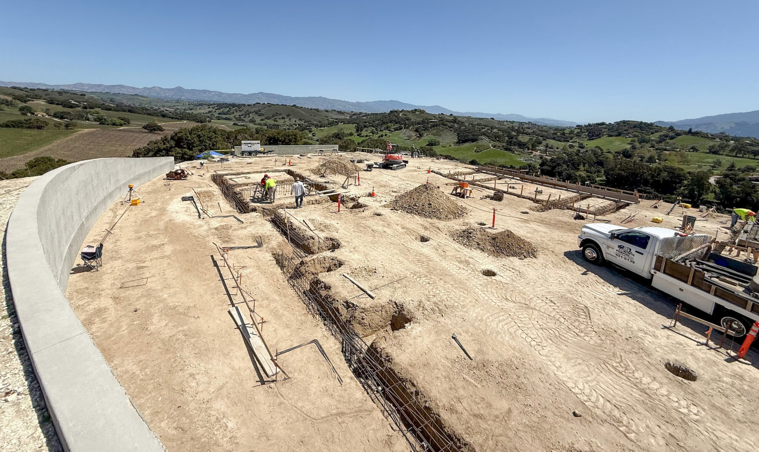 Hygge House construction site showing foundation work and the curved concrete retaining wall.
