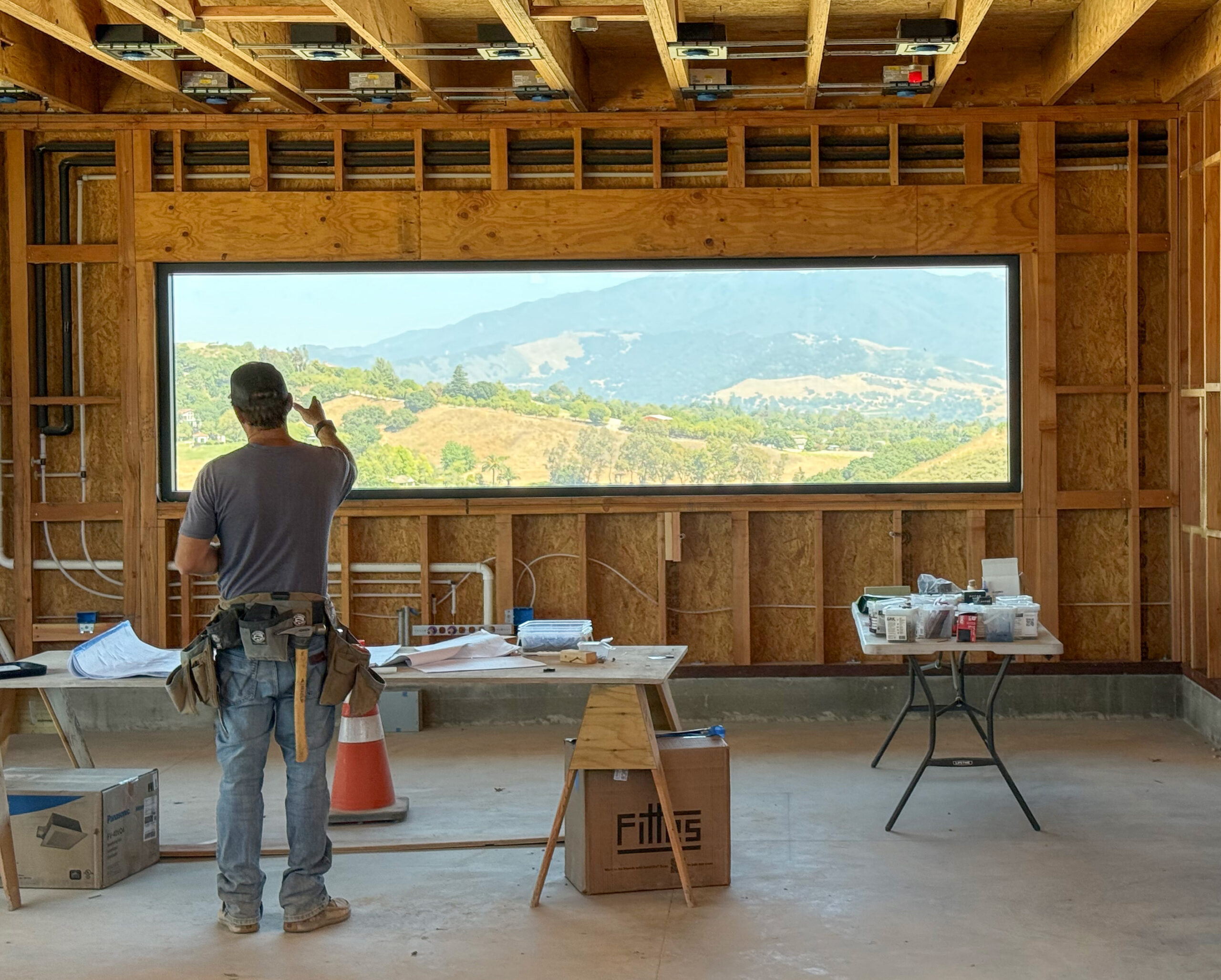 Hygge House interior under construction with a large picture window framing views of the surrounding hills.